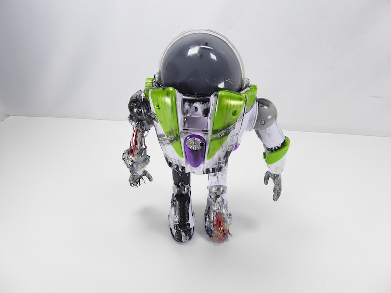 May include: A Buzz Lightyear action figure with a clear plastic body, green and purple accents, and a dark gray helmet. The figure has articulated limbs and a detailed design, showcasing a futuristic space ranger aesthetic.
