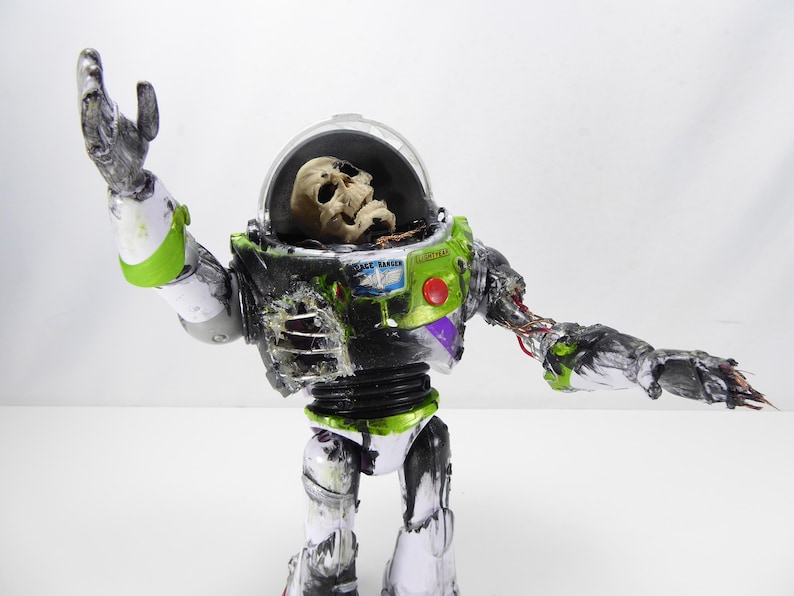 May include: A modified Buzz Lightyear action figure with a skull inside the helmet. The toy is painted in green, white, and black with visible damage and exposed wiring. The figure's arm is outstretched.