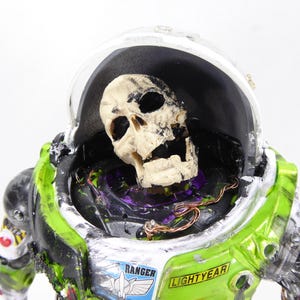 May include: A green and white Buzz Lightyear costume with a skull inside the helmet. The costume has the word "Ranger" and "Lightyear" printed on it. The skull is off-white and the costume has a distressed look.