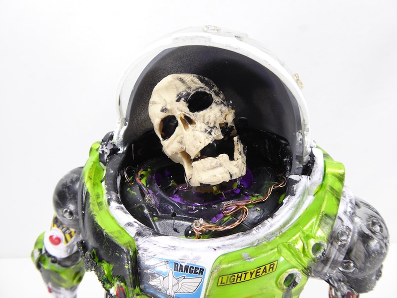 May include: A green and white Buzz Lightyear costume with a skull inside the helmet. The costume has the word "Ranger" and "Lightyear" printed on it. The skull is off-white and the costume has a distressed look.
