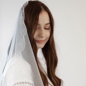 Pode incluir: Um véu de noiva branco com delicados desenhos florais bordados. O véu é feito de um tecido macio e transparente, perfeito para uma cerimônia de casamento.