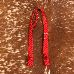 May include: A bright red braided halter with a silver-colored buckle. The halter is made of a thick, woven material and is designed to be placed on a horse's head. The background is a brown and white spotted pattern.