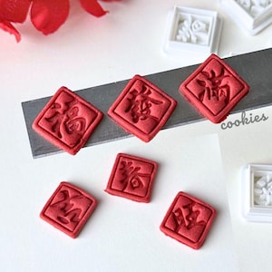 May include: Red clay cutters with Chinese blessing imprints, and white square molds. The image includes red floral accents and the text "Chinese Blessing Clay Cutter with Imprint."