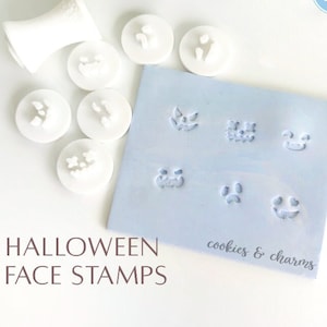 May include: White Halloween face stamps with a handle, alongside a light blue pad with stamped faces. The text "Halloween Face Stamps" is visible. The stamps feature various jack-o'-lantern and spooky face designs.