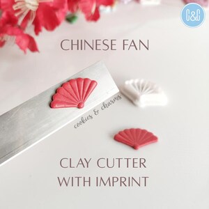 May include: A clay cutter with an imprint of a red Chinese fan. The cutter is on a silver metal surface. The text "Chinese Fan" and "Clay Cutter with Imprint" is visible in the image.