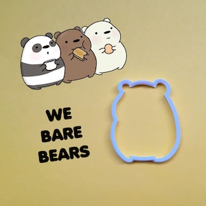 May include: A set of three We Bare Bears cookie cutters. The cutters are shaped like the three bears from the cartoon: Panda, Grizzly, and Ice Bear. The cutters are made of blue plastic and are on a light brown background.