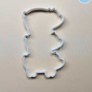May include: White plastic cookie cutter shaped like a cartoon bear standing on its hind legs.
