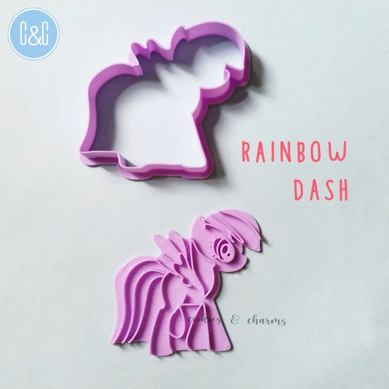 Puede incluir: Cortador de galletas de pl&aacute;stico morado con forma de Rainbow Dash de My Little Pony. El cortador est&aacute; en dos piezas, una para el contorno y otra para los detalles. El texto "RAINBOW DASH" est&aacute; impreso sobre un fondo blanco.
