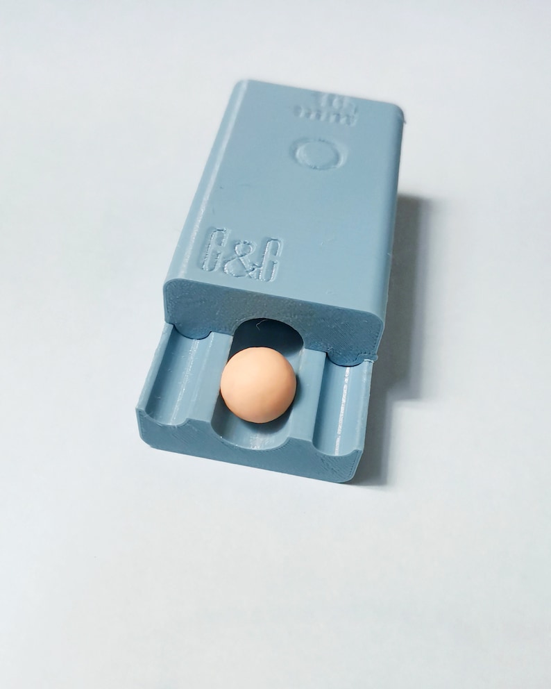 May include: A light blue plastic box with a small, round, light brown object inside. The box has the text "G&G" and "10 mm" printed on it.