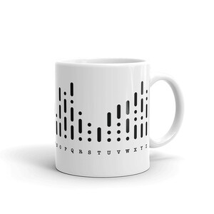 May include: White ceramic mug with a black graphic of a stylized alphabet in braille. The letters O through Y are printed below the graphic.