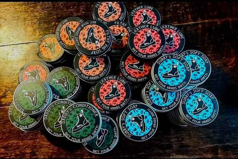 May include: A collection of round, colorful stickers with various designs featuring boots, text, and leopard print patterns. The stickers have black borders and white text that reads "Get Your Hands Dirty" and "Subby's Soft Soap".