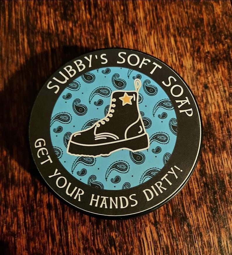 May include: A black and white circular sticker with a blue paisley pattern. The sticker features a black boot with a yellow star and the text "Subby's Soft Soap Get Your Hands Dirty!"