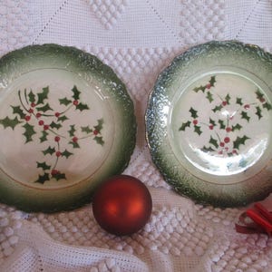 May include: Two white ceramic plates with green and gold trim. The plates feature a design of holly leaves and red berries.