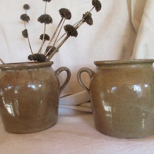 May include: Two brown ceramic crocks with handles. The crocks are glazed and have a rustic look.
