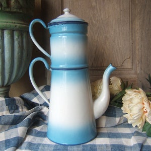 May include: A blue and white enamel coffee pot with a double filter. The pot has a spout and two handles. It is sitting on a blue and white checkered tablecloth.