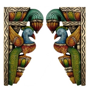 May include: A pair of hand-carved wooden wall brackets featuring symmetrical peacock motifs. Each bracket is painted in vibrant shades of green, blue, yellow, and orange, with intricate textured patterns along the vertical edges and scrollwork.