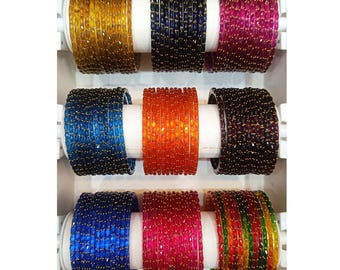 Puede incluir: Un conjunto de pulseras de cristal de colores con detalles dorados. Las pulseras están dispuestas en tres filas de seis, cada fila con un color diferente. Los colores incluyen dorado, azul, rojo, naranja, negro y verde.