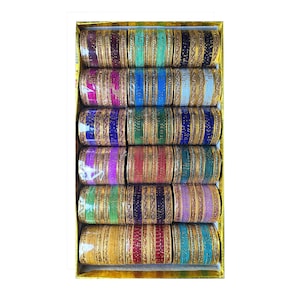 May include: A box filled with multiple sets of colorful bangles. The bangles are arranged in rows, showcasing a variety of colors including gold, green, blue, red, and purple. Each bangle set has a gold-colored band with intricate detailing.