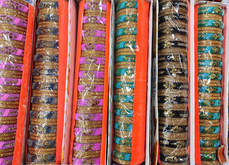 Puede incluir: Surtido de pulseras coloridas en varios tonos de rosa, azul, verde y negro. Las pulseras est&aacute;n apiladas en filas y presentan detalles dorados y dise&ntilde;os intrincados.