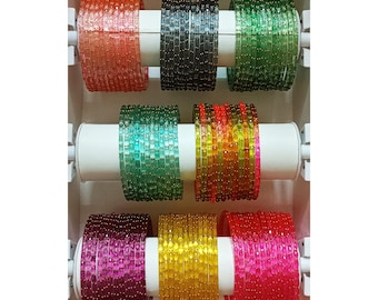 Puede incluir: Un conjunto de ocho pulseras de vidrio de colores con un diseño de cuentas. Las pulseras están dispuestas en un patrón de arcoíris, con cada pulsera de un color diferente. Las pulseras se muestran en un soporte blanco.