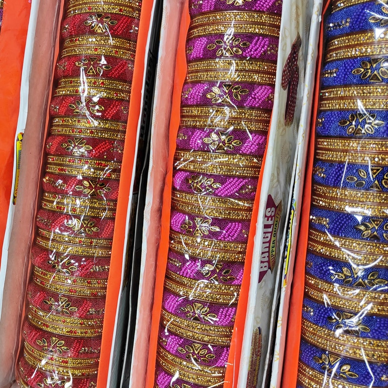 Puede incluir: Un conjunto de tres pulseras coloridas con dise&ntilde;os intrincados. Las pulseras est&aacute;n hechas de cuentas de vidrio y tienen un borde dorado. Las pulseras est&aacute;n dispuestas en una fila, con las pulseras rojas a la izquierda, las pulseras moradas en el medio y las pulseras azules a la derecha. Las pulseras se muestran sobre un fondo blanco con el texto "Bangles" y "Super Quality" impreso en el embalaje.
