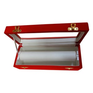 May include: Open red velvet jewelry box with a clear glass top and gold-colored clasps. The interior features a white roller for displaying bracelets or necklaces. The box is designed to showcase and protect jewelry.