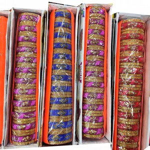 Puede incluir: Surtido de pulseras coloridas en cajas. Las pulseras son de pl&aacute;stico y tienen un borde dorado. Las cajas son de color naranja y blanco.