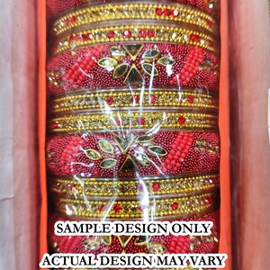 Puede incluir: Un conjunto de brazaletes rojos y dorados con dise&ntilde;os intrincados y adornos. Los brazaletes est&aacute;n envueltos en pl&aacute;stico y tienen una etiqueta que indica que es solo un dise&ntilde;o de muestra. El texto de la etiqueta dice: "SAMPLE DESIGN ONLY ACTUAL DESIGN MAY VARY BUT WILL CONTAIN SAME STONES/BEADS/DESIGNER LOOK 100% SATISFACTION GUARANTEED"