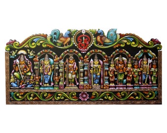 Puede incluir: Un tapiz de pared de madera colorido con intrincados tallados que representan deidades hindúes. Las deidades están pintadas en colores vibrantes y están dispuestas en una fila debajo de un arco decorativo. El tapiz de pared está adornado con motivos florales y un símbolo del dios hindú Shiva.