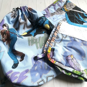 Può includere: Una borsa in tessuto blu e nero a tema Batman e Joker. La borsa ha una chiusura a coulisse ed è realizzata in tessuto morbido e trapuntato.