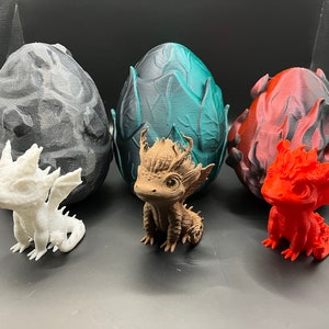 May include: Three small dragon figurines, each in a different color, sitting in front of their corresponding eggs. The eggs are made of a textured material and are painted in shades of gray, teal, and red. The dragons are white, brown, and red.