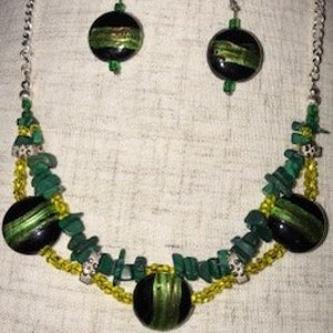 May include: A green and black necklace and earrings set with round beads and a silver chain. The necklace features a layered design with green and yellow beads.