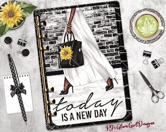 May include: A black and white planner with gold accents and the text "today is a new day." The planner features an illustration of a woman with a black handbag adorned with a sunflower. A cup of green tea and a sunflower are also visible.