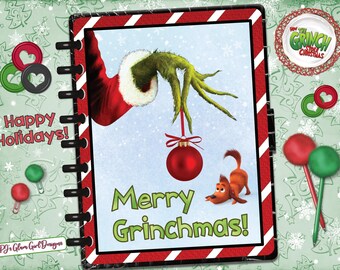 May include: A holiday-themed notebook with a red and white striped border. The cover features the Grinch's hand holding a red ornament, with Max the dog. The text "Merry Grinchmas!" is displayed in green. The words "Happy Holidays!" are also visible.