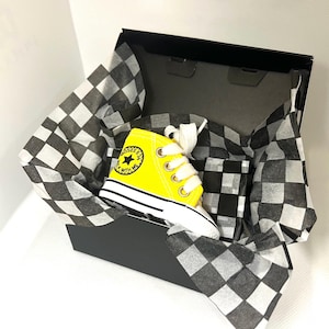Puede incluir: Una zapatilla alta amarilla con cordones blancos, presentada en una caja a cuadros blancos y negros. La zapatilla tiene una suela blanca y el texto "ROSES & ME WALK WITH ME" en el lateral.
