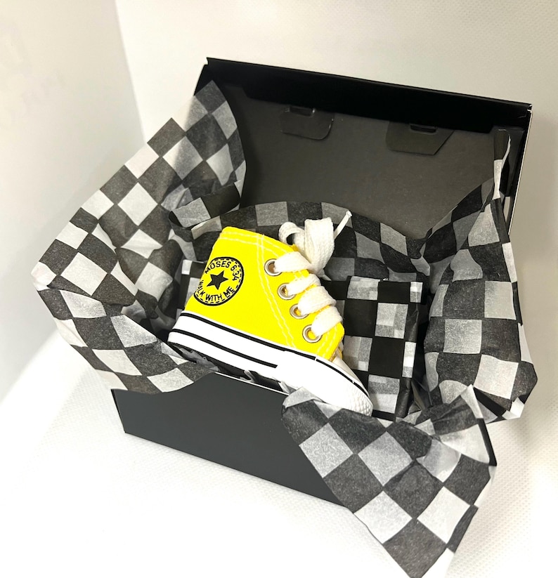 Puede incluir: Una zapatilla alta amarilla con cordones blancos, presentada en una caja a cuadros blancos y negros. La zapatilla tiene una suela blanca y el texto "ROSES & ME WALK WITH ME" en el lateral.