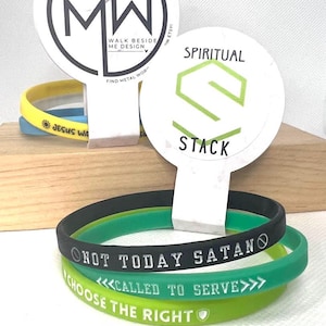 May include: A stack of rubber bracelets in black, green, and yellow. The black bracelet reads "NOT TODAY SATAN". The green bracelet says "CALLED TO SERVE". The yellow bracelet says "CHOOSE THE RIGHT".