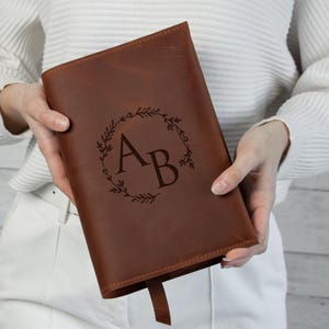 Puede incluir: Un diario de cuero marrón con un diseño de corona floral y las iniciales "AB" grabadas en la parte delantera.
