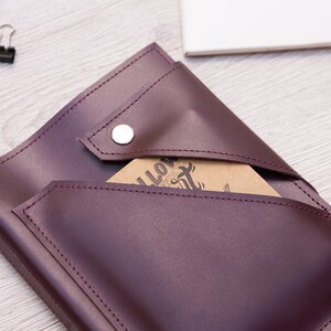 May include: Burgundy leather journal with a flap closure and a snap button. The journal has a pocket on the front and the initials "SR" are embossed on the front cover.