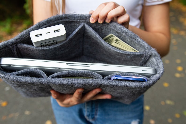 May include: A grey felt organiser with multiple pockets, holding a laptop, a phone, a power bank, and cash. The organiser is open and the items are visible.