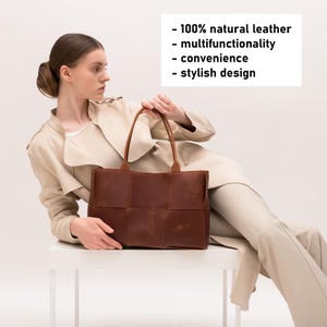 May include: A brown leather tote bag with a woven design. The bag is being held by a person wearing a beige coat and pants. The text on the image reads: - 100% natural leather - multifunctionality - convenience - stylish design