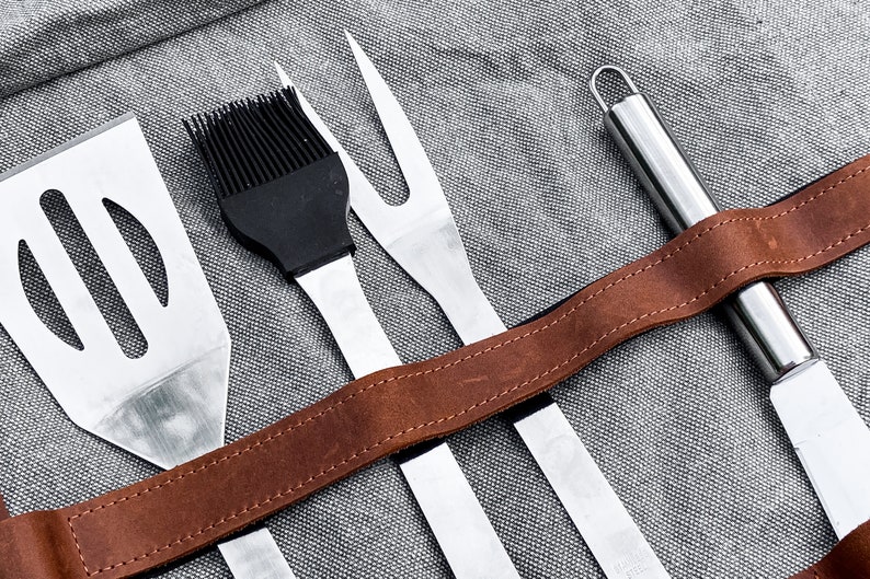 以下が含まれることがあります： 茶色の革ひもが付いた4つのグリル用具のセット。道具には、ヘラ、塗りブラシ、フォーク、ナイフが含まれています。