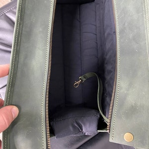 May include: A green leather bag with a zip closure and a brass clasp. The bag is lined with a dark fabric and has a small pocket on the inside.