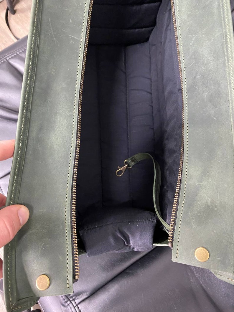 May include: A green leather bag with a zip closure and a brass clasp. The bag is lined with a dark fabric and has a small pocket on the inside.
