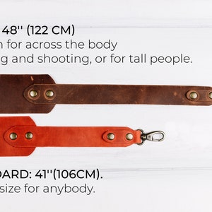 Peut inclure: Deux sangles de cam&eacute;ra en cuir, l'une brune et l'autre orange, avec des fermoirs m&eacute;talliques. La sangle brune est &eacute;tiquet&eacute;e "LONG: 48" (122 CM)" et la sangle orange est &eacute;tiquet&eacute;e "STANDARD: 41" (106CM)."