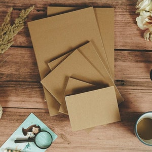 Puede incluir: Un conjunto de cinco cuadernos de papel marr&oacute;n de diferentes tama&ntilde;os apilados sobre una superficie de madera. Los cuadernos est&aacute;n hechos de papel reciclado y tienen un aspecto natural y r&uacute;stico.