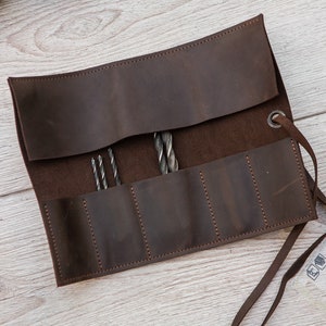 May include: A brown leather roll with six slots for holding drill bits. The roll has a tie closure and is made of distressed leather.