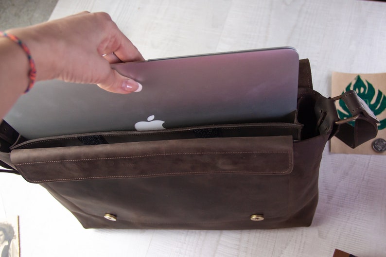 May include: A brown leather messenger bag with a laptop inside. The bag has a flap closure and a shoulder strap.