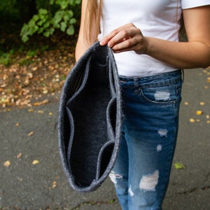 May include: A grey felt organiser with multiple compartments, held open by a person's hand.