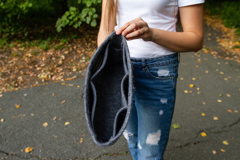 May include: A grey felt organiser with multiple compartments, held open by a person's hand.
